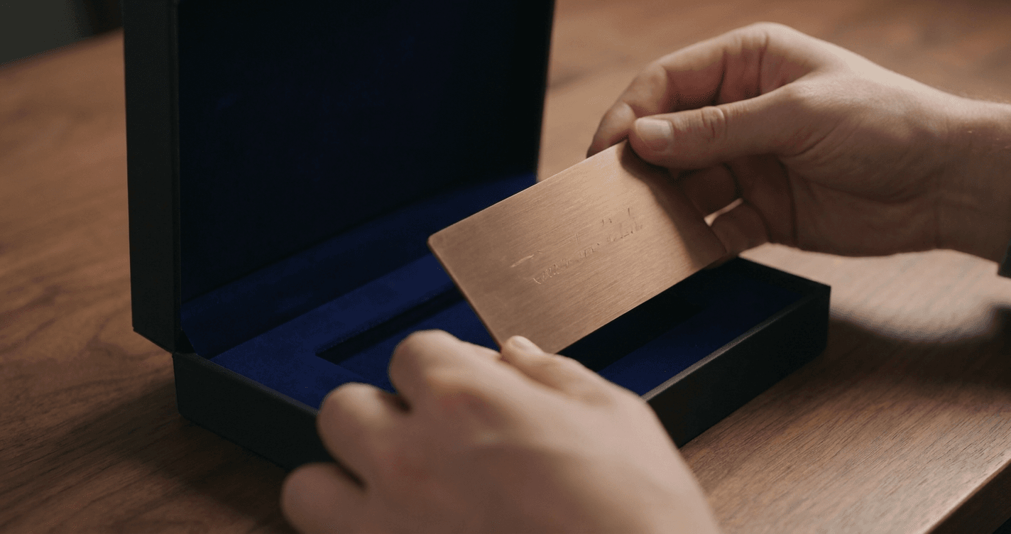 Hands carefully lifting a custom-engraved brushed bronze commemorative piece from a velvet-lined matte presentation box.